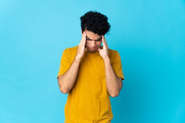 Genç Venezuelalı adam mavi arka planda baş ağrısı ile izole edilmiş.