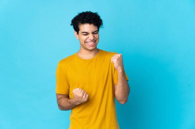 Genç Venezuelalı bir adam mavi arka planda izole edilmiş zaferi kutluyor.