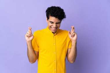 Genç Venezuelalı adam mor arka planda izole edilmiş ve şans diliyor.