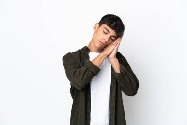 İzole edilmiş beyaz arka planda genç bir adam uyku jesti yapıyor.