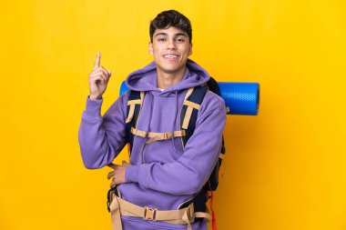 Sarı arka planda büyük bir sırt çantası olan genç dağcı harika bir fikre işaret ediyor.