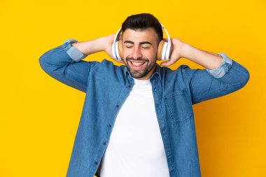 İzole edilmiş sarı arka planda beyaz bir adam müzik dinliyor.