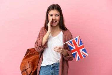 Young caucasian woman holding an United Kingdom flag isolated on pink background shouting with mouth wide open
