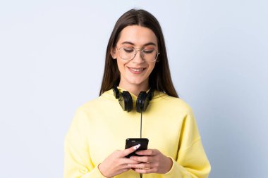 Soyutlanmış mavi arka plan müzik dinleyen ve cep telefonu arayan genç bir kadın.