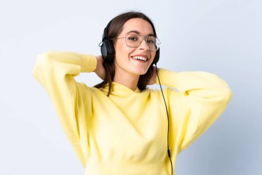 Soyutlanmış mavi arka planda müzik dinleyen genç bir kadın.