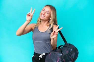 Young sport woman with sport bag isolated on blue background showing victory sign with both hands