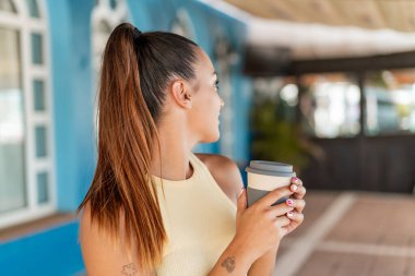 Dışarıdaki güzel kadın elinde kahve tutuyor.