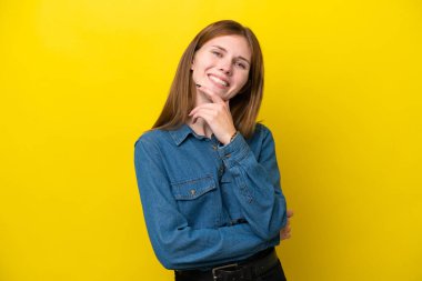 Sarı arka planda izole edilmiş genç İngiliz kadın mutlu ve gülümsüyor.