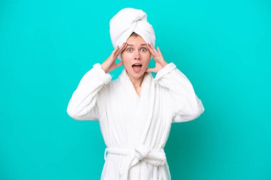 Bornozlu genç bir kadın mavi arka planda izole edilmiş, sürpriz bir ifadeyle.