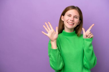 Mor arka planda izole edilmiş genç İngiliz kadın parmaklarıyla yediyi saydı