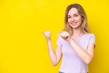 Blonde English young girl isolated on yellow background pointing to the side to present a product
