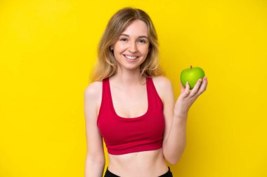Sarışın İngiliz genç kız, sarı arka planda bir elmayla izole edilmiş.