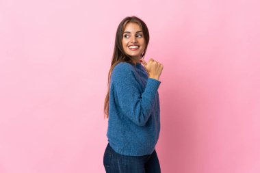 Pembe arka planda izole edilmiş genç Uruguaylı kadın bir ürünü sunmak için kenarı işaret ediyor.
