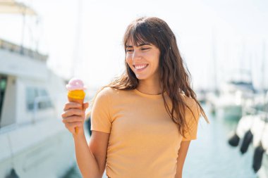 Açık havada kornet dondurmalı genç bir kadın, neşeli bir ifadeyle.