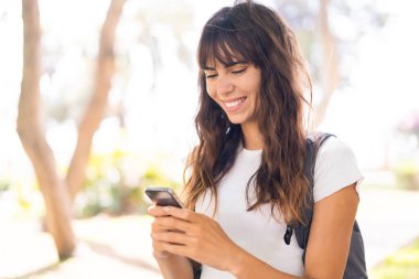 Açık havada cep telefonu kullanan genç bir kadın.