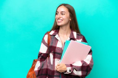 Young student caucasian woman isolated on blue background looking to the side and smiling