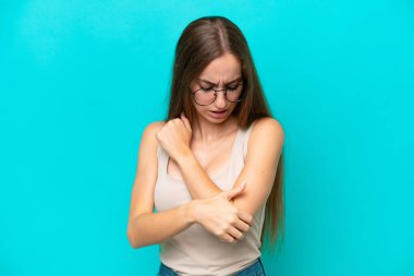 Genç beyaz kadın, mavi arka planda izole edilmiş, dirsek ağrısı var.