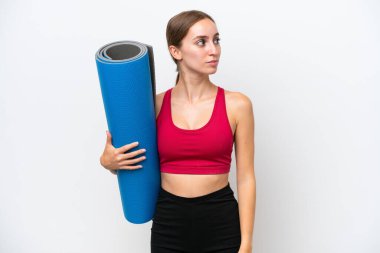 Beyaz arka planda izole edilmiş bir minder tutarken yoga derslerine giden beyaz tenli genç bir kadın.