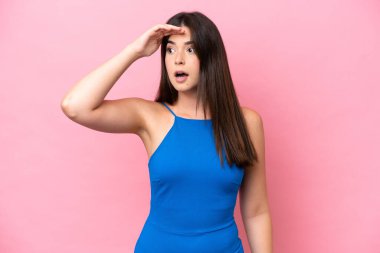 Genç Brezilyalı bir kadın pembe arka planda izole edilmiş. Sürpriz bir ifadeyle yan tarafa bakıyor.