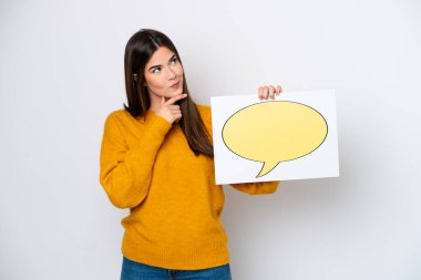 Young Brazilian woman isolated on white background holding a placard with speech bubble icon and thinking