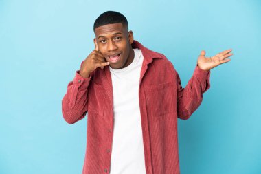 Genç latin adam mavi arka planda izole edilmiş telefon jestleri yapıyor ve şüphe ediyor