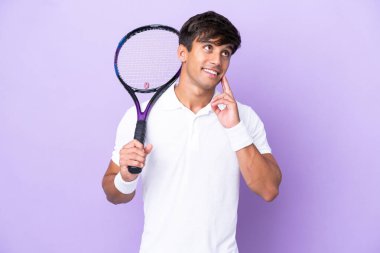 Handsome young tennis player man isolated on ocher background thinking an idea while looking up