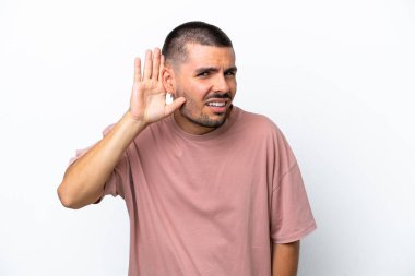 Beyaz arka planda izole edilmiş genç beyaz bir adam. Kulağına elini sürerek bir şeyler dinliyor.