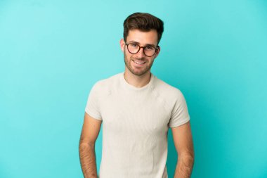 Genç beyaz yakışıklı adam mavi arka planda izole edilmiş gülüyor.