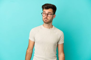 Mavi arka planda soyutlanmış beyaz, yakışıklı genç bir adam şüpheli hareketler yapıyor.