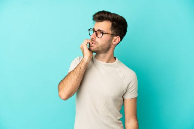 Mavi arka planda izole edilmiş beyaz, yakışıklı genç bir adam biraz gergin.