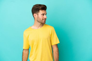 Beyaz tenli yakışıklı adam mavi arka planda izole edilmiş, yana bakıyor ve gülümsüyor.