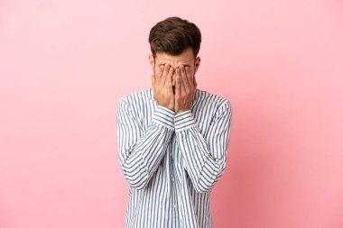 Pembe arka planda izole edilmiş, yorgun ve hasta bir ifadeyle genç, beyaz, yakışıklı bir adam.