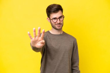 Sarı arka planda izole edilmiş genç beyaz adam mutlu ve parmakları olan dört kişi sayıyor.
