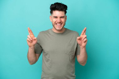 Genç beyaz adam mavi arka planda izole edilmiş ve şans diliyor.