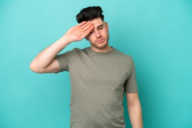 Kafkasyalı genç adam mavi arka planda izole edilmiş, yorgun ve hasta bir ifadeyle.