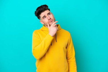 Kafkasyalı genç adam mavi arka planda izole edilmiş. Şüpheleri var.