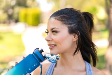 Dışarıda bir şişe suyla spor yapan genç ve güzel bir kadın.