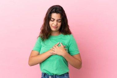 Pembe arka planda izole edilmiş, kalbinde ağrı olan beyaz bir kadın.