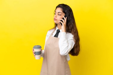 Kafkas lokantası garsonu sarı arka planda izole edilmiş. Elinde kahve ve cep telefonu var.