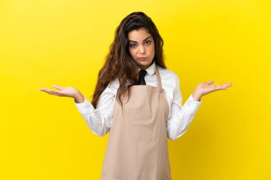 Kafkas restoranındaki genç garson sarı arka planda izole edilmiş. El kaldırırken şüpheleri var.