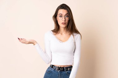 Tecrit edilmiş bej arka planı olan genç bir kadın şüpheli hareketlerde bulunuyor.