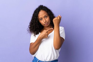 Kübalı genç bir kız, mor arka planda izole edilmiş, geç kalma jesti yapıyor.