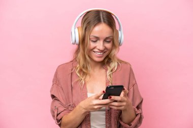 Genç Rus kadın pembe arka planda izole edilmiş müzik dinliyor ve cep telefonu arıyor.