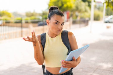 Açık havada genç ve güzel bir bayan omuzlarını kaldırırken şüpheyle hareket ediyor.