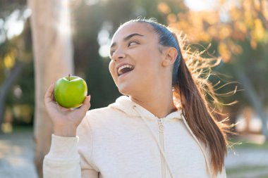 Genç, güzel, spor bir kadın elinde mutlu bir ifadeyle bir elma tutuyor.