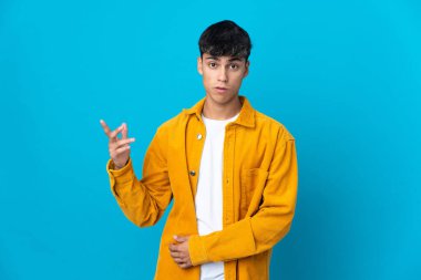 Soyutlanmış mavi arka planı olan genç bir adam şüpheli hareketler yapıyor.