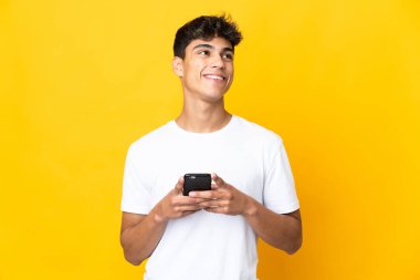 Sarı arka plan izole edilmiş genç adam cep telefonu kullanıyor ve...