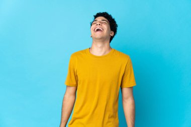 Genç Venezuelalı adam mavi arka planda izole edilmiş gülüyor.