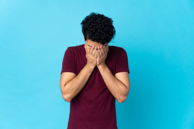 Genç Venezuelalı adam mavi arka planda izole edilmiş, yorgun ve hasta bir ifadeyle.