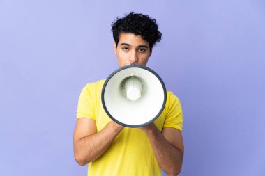 Genç Venezuelalı bir adam mor arka planda izole edilmiş bir şekilde megafondan bir şey duyurmak için bağırıyor.